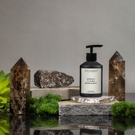 Lotion bottle with pump on a stone surface surrounded by crystals and greenery
