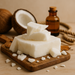 Stack of white soap bars on a wooden board with coconuts and a bottle in the background.