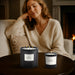 Woman sitting on a couch with two lit Baies Candles 