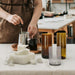 Person working with candles and glass containers on a table in a kitchen setting